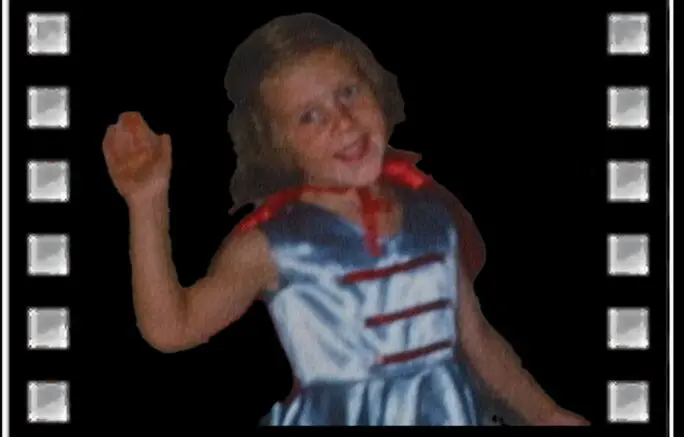 A young girl in a dress waving at the camera.